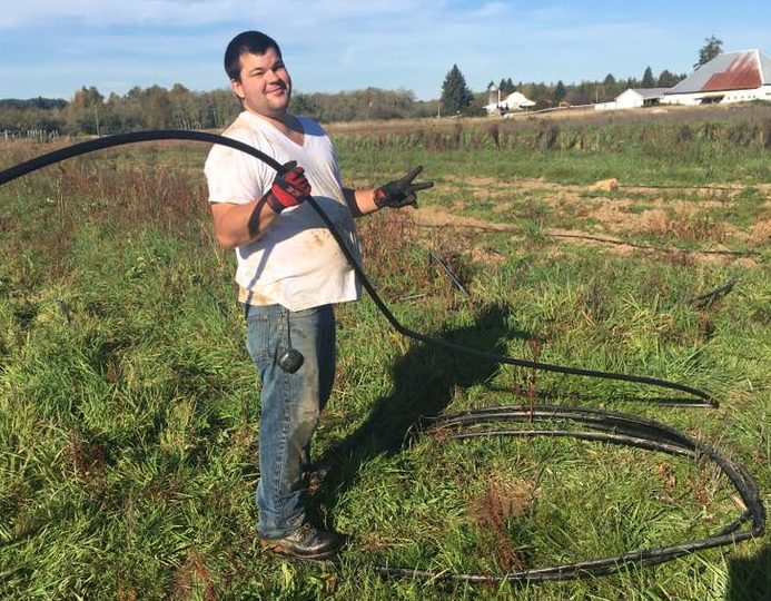 A young man standing out in a field, holding irrigation tubing